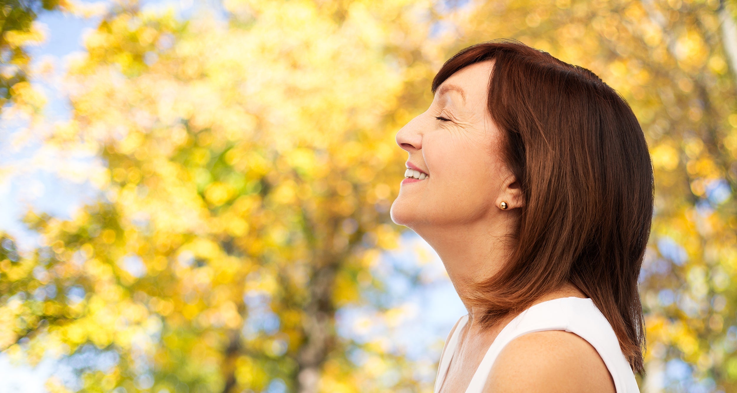 A mature woman stands amid autumn trees. If you're wondering how to sleep after a rhinoplasty, check out our comprehensive guide and boost your recovery and investment with a safe and secure night's sleep.
