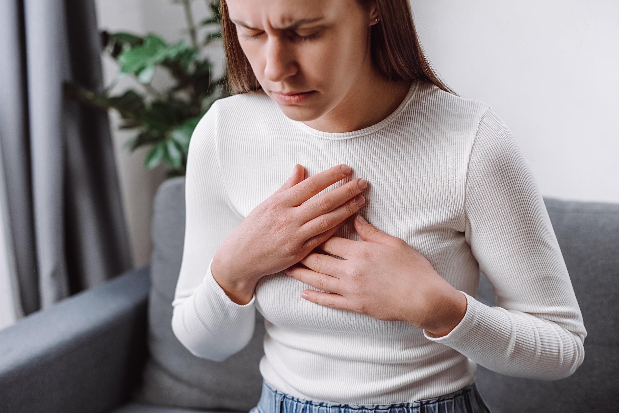A woman clutches her chest. Tired of waking up with burning chest pain? Learn the best sleep positions and elevation techniques to stop nighttime acid reflux and finally sleep peacefully.