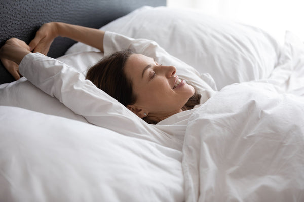 A woman wakes up feeling refreshed after sleeping. If you're looking for how to train yourself to sleep on your back, we've got you covered with our comprehensive guide on how to make the transition to back sleeping.