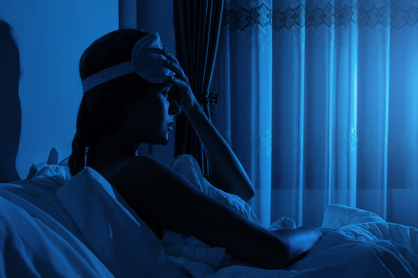 A woman struggles with insomnia while in bed. Insomnia after surgery is extremely common. Get the healing rest you need and deserve in our full guide.