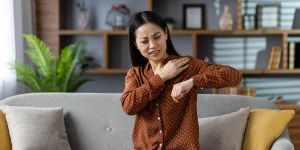 A woman rubs her shoulder in pain. Our ultimate guide to pillows for shoulder pain shares the reasons behind shoulder pain and how to prevent it once and for all with the right shoulder pain pillow.