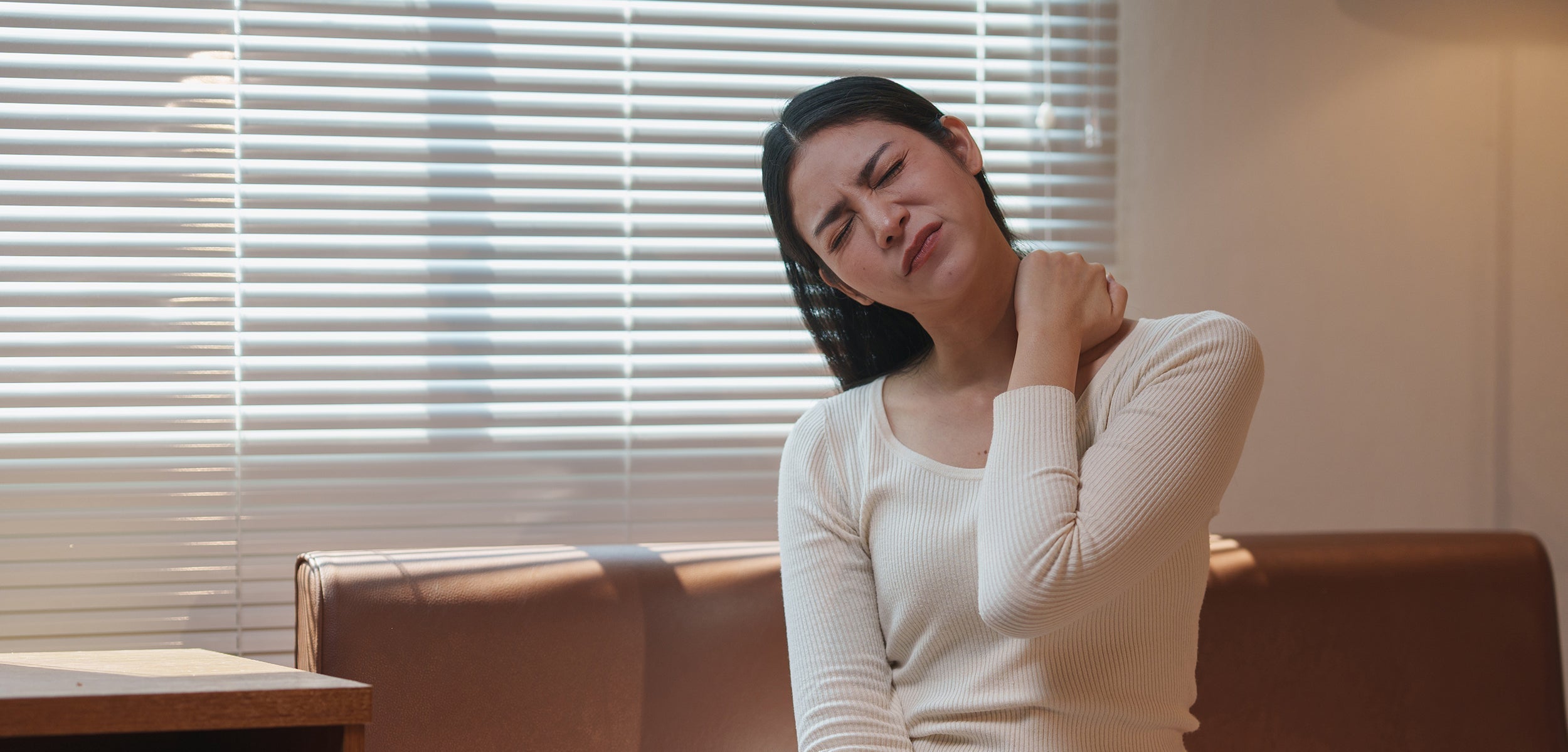 A woman clutches her neck in pain. If you're experiencing rhomboid pain, learn how your sleep position can help.