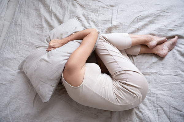 A woman curls up in pain in bed. Sleeping with Piriformis Syndrome pain can be seriously challenging. Learn more on how to get relief in our complete guide.
