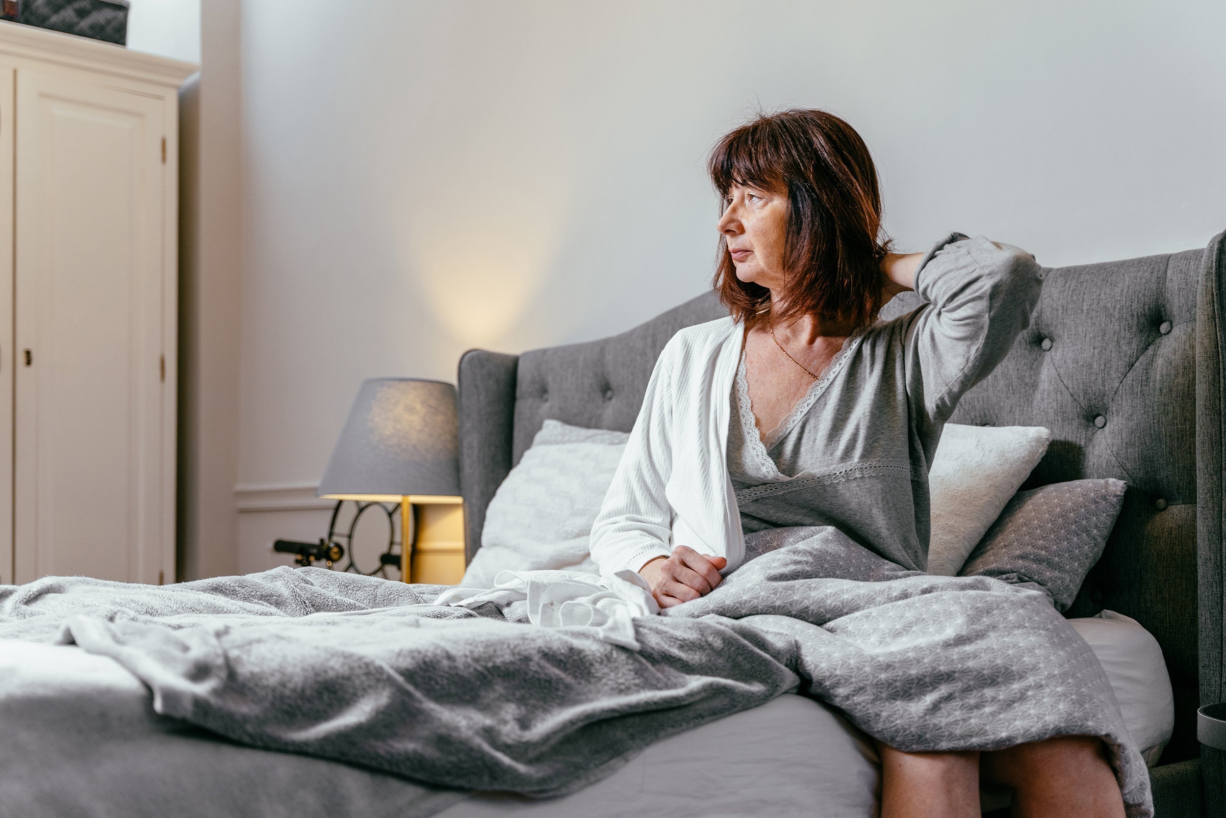 A woman sits up in bed. How to sleep comfortably with tissue expanders: proper elevation angles, safe side sleeping transitions, and positioning support that adapts as expanders fill.