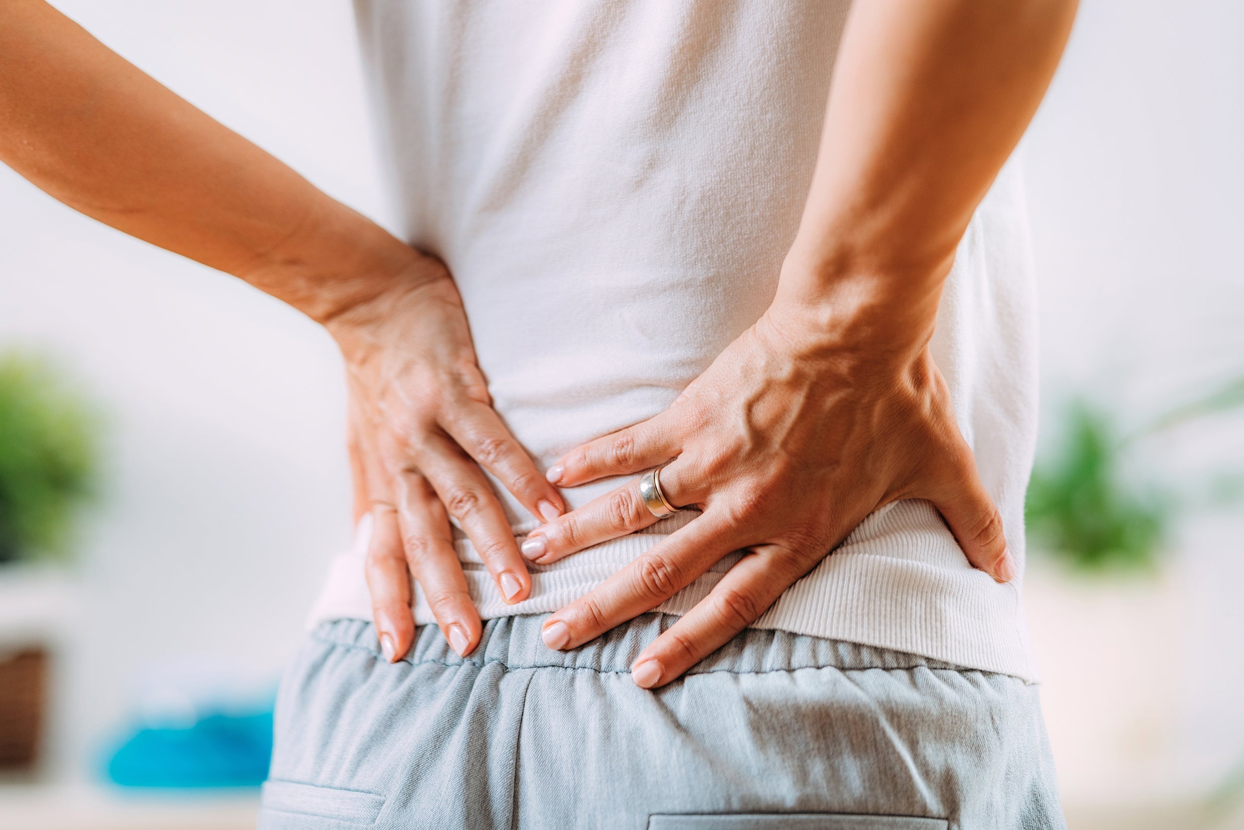 A woman clutches her SI joint area in pain. If you're suffering from sacroiliac joint pain, read our comprehensive article on how to get relief, especially when sleeping.