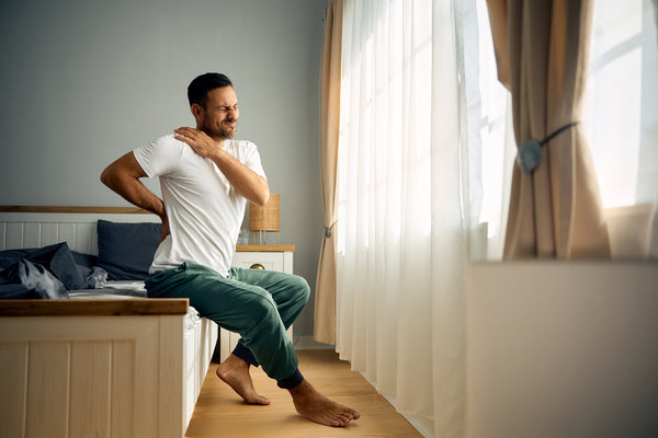 A man clutches his upper shoulder in bed. Discover the best sleeping position for Thoracic Outlet Syndrome and actually get some rest without waking up with numb arms.