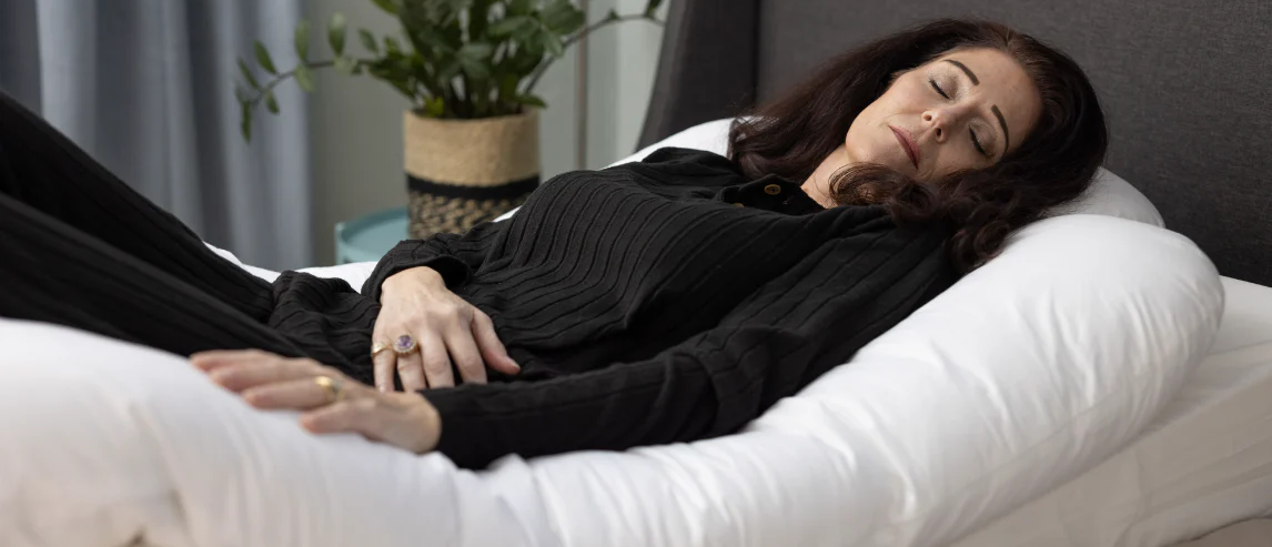A woman sleeps in bed using the Sleep Again Pillow System, a full-body pillow system designed to support elevated sleeping after a mastectomy.