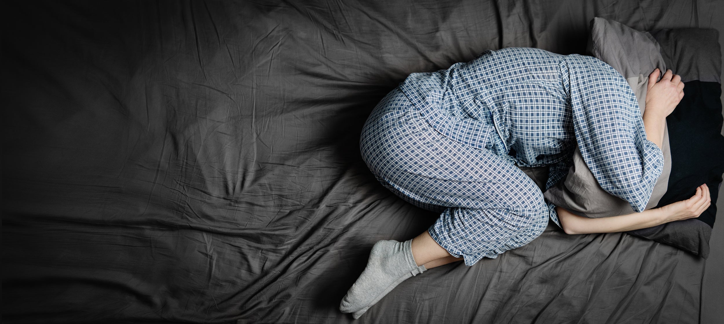 A person curls up in a ball while sleeping. If you're struggling to sleep with shingles, explore out complete guide on why shingles pain is worse at night and how you can get relief.
