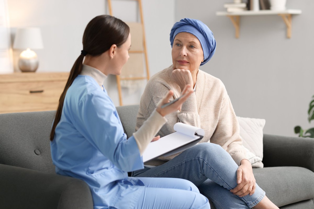 Woman with bonnet siting with woman with scrubs and a clipboard.