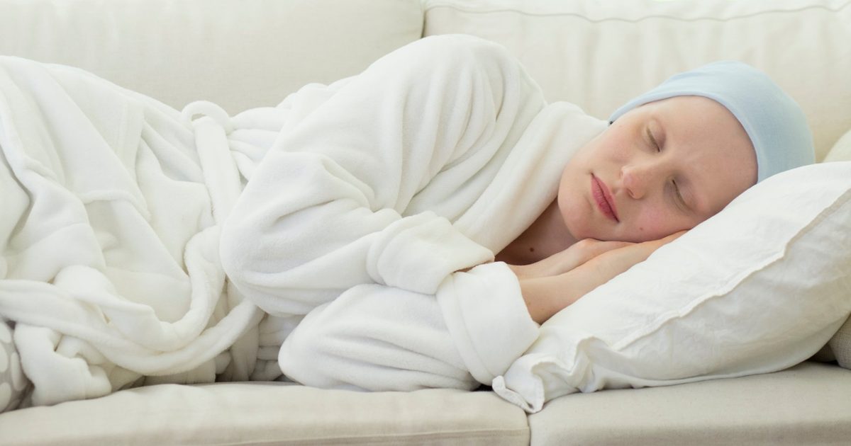Person sleeping on a sofa in a white robe and light blue head cover.
