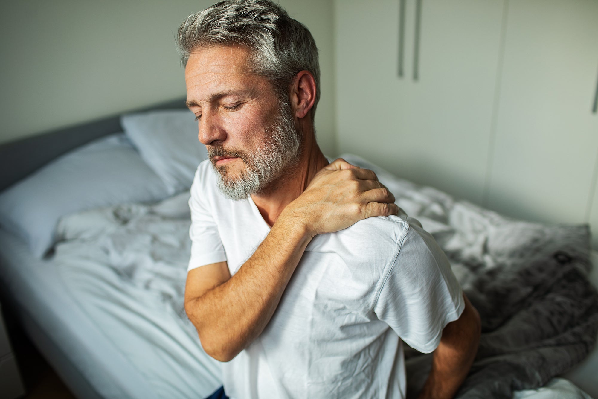 A man with shoulder pain. Frozen shoulder pain waking you up at night? Learn the best sleep positions, proper pillow support, and how to prep before surgery for real, lasting relief.