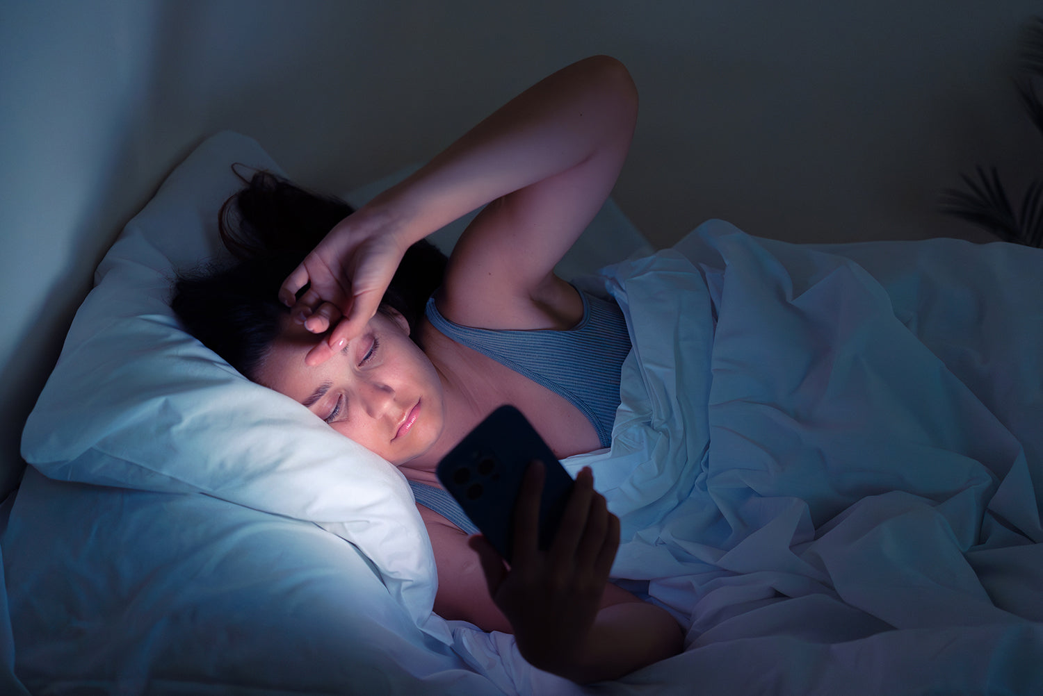 A woman reads her phone in bed. Back sleeping is normally restricted after BBL, but a suspended positioning setup removes the pressure risk. See how to sleep on your back safely during recovery.