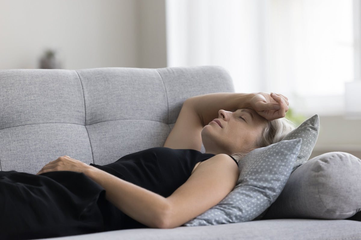 A woman laying on the couch with the back of her hand on her forehead.