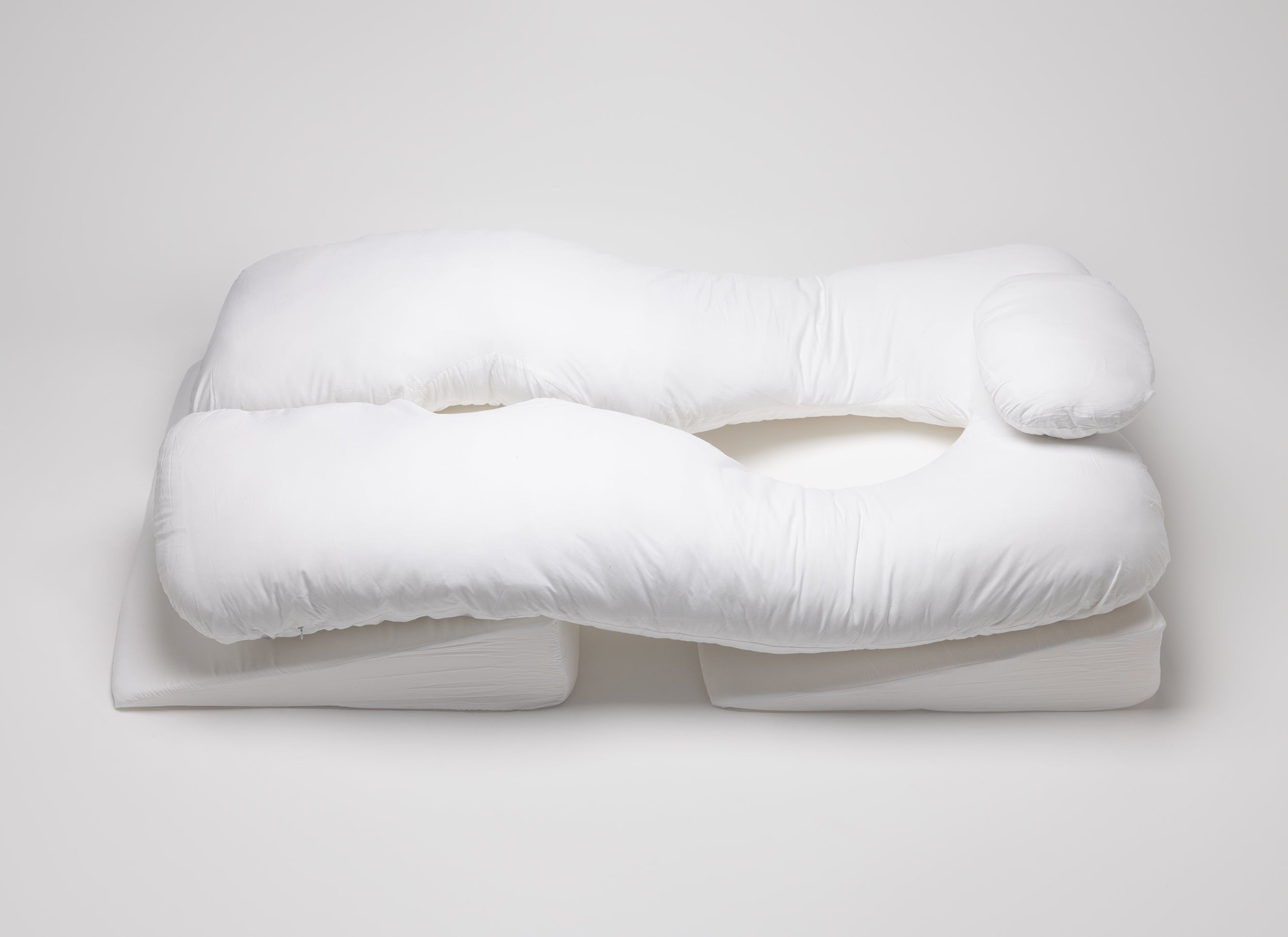 A large, white, U-shaped body pillow with a headrest rests on two rectangular foam pads, all on a plain white background.