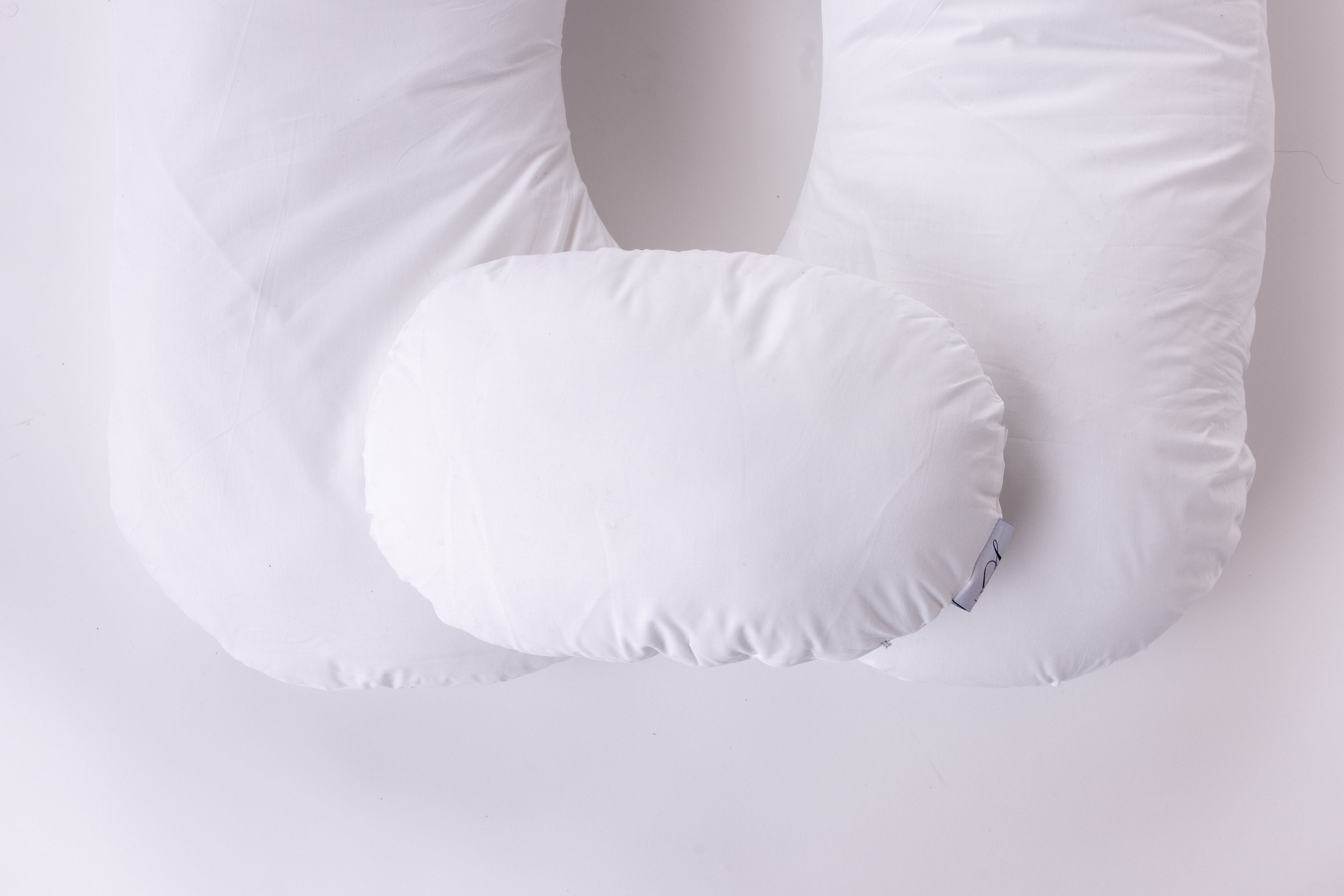 A large, white U-shaped pillow with an attached smaller oval pillow, designed for contoured bedding comfort, is shown on a plain white background. Two side pillows are not included and are sold separately.