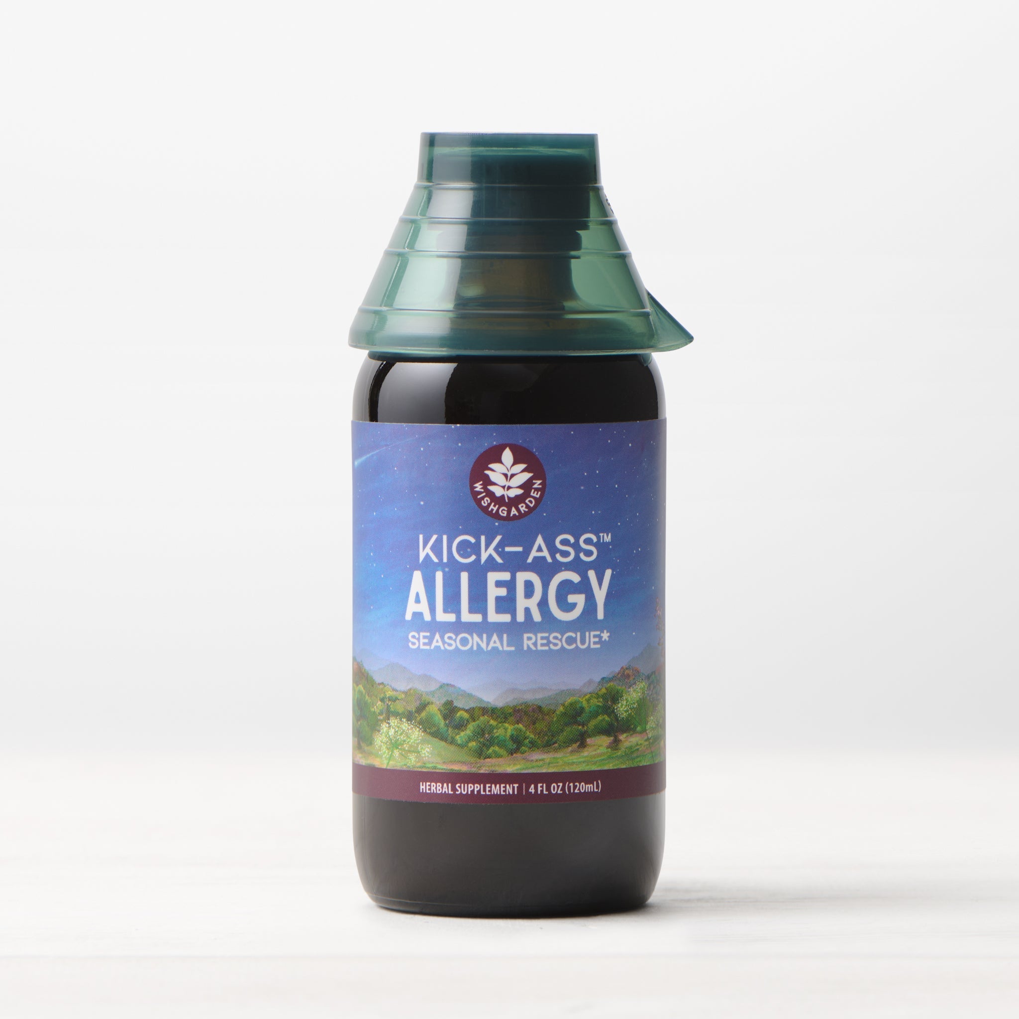 A bottle of Kick-Ass Allergy, Seasonal Rescue tincture featuring a blue and purple label with a mountain design and green cap, displayed on a light surface against a plain background.