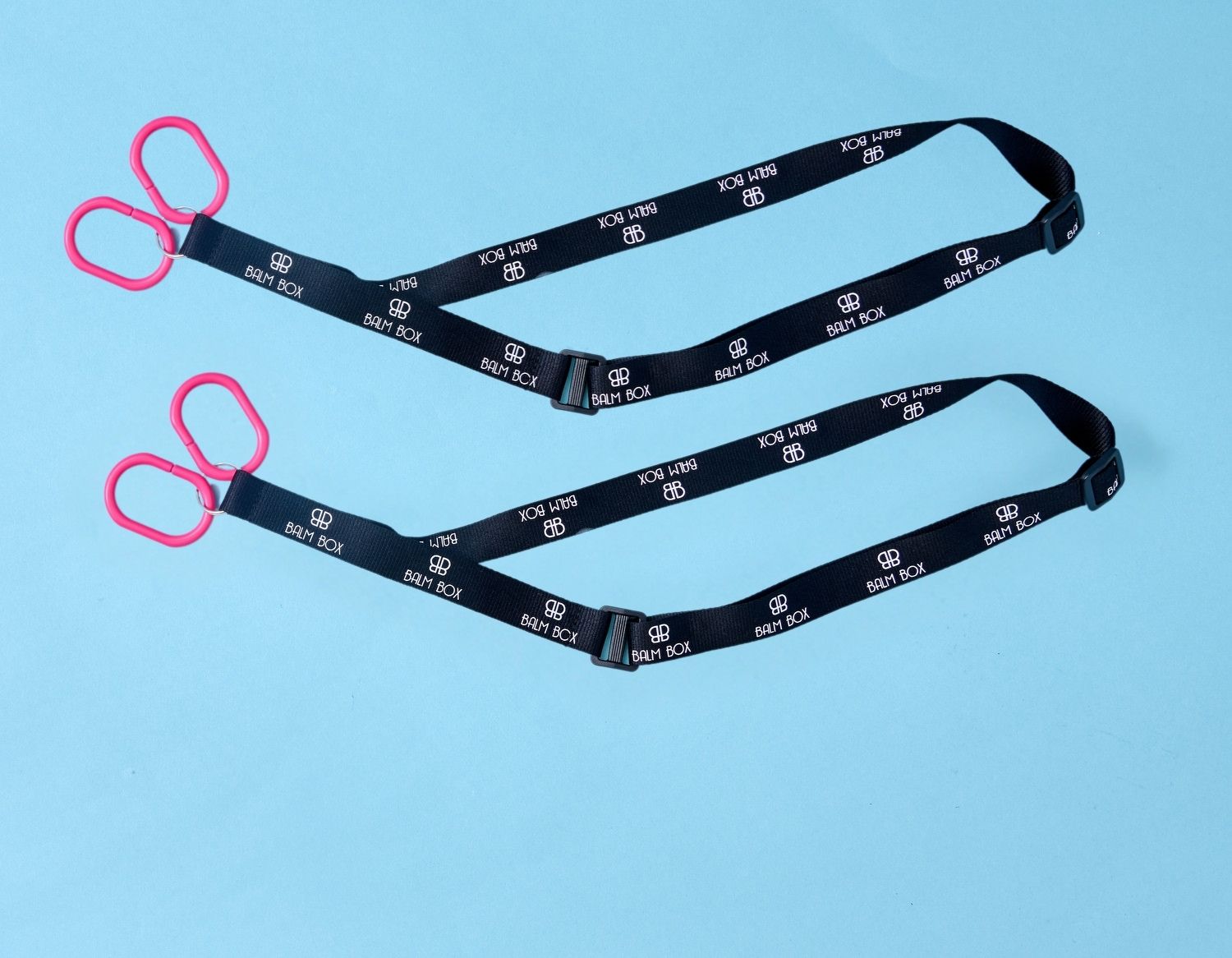 Two black straps with white text and logos, each ending in a pair of red plastic handles, are laid out on a light blue background—perfect for use as the Surgical Drain Holder.