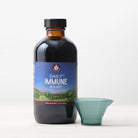 A bottle of Daily Immune Builder with a blue measuring cup sits on a white surface against a plain light background, highlighting this herbal supplement for daily immune support.