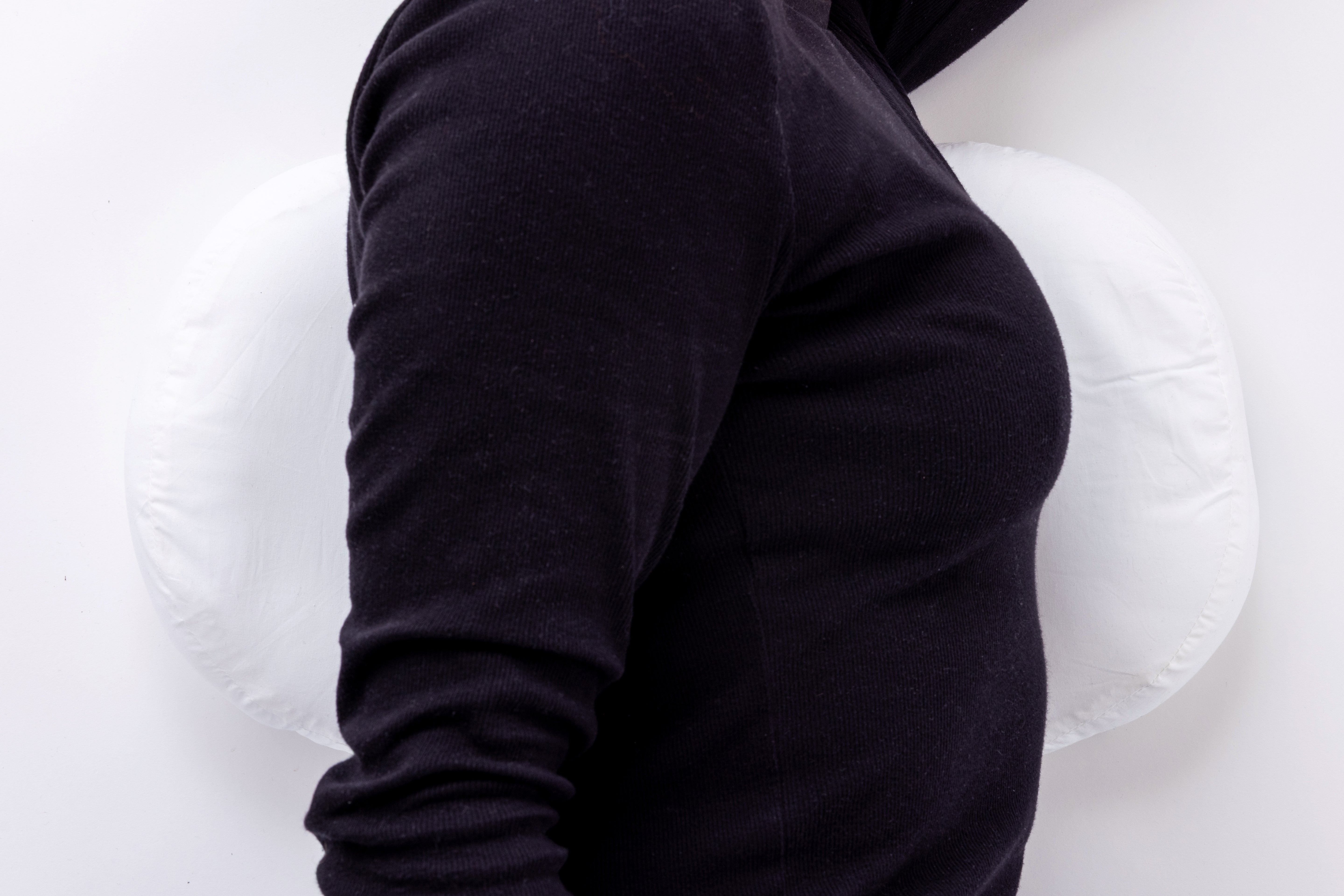 A person in a black long-sleeve shirt uses the Side Sleeping Chest Pillow, sitting with their back against its white, round design for lower back comfort. The background is plain white.