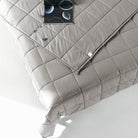 A minimal, modern bed features the Pillowtex Weighted Blanket in light grey, quilted and filled with glass beads. An open book and eyeglasses rest on the corner of the neatly made bed.