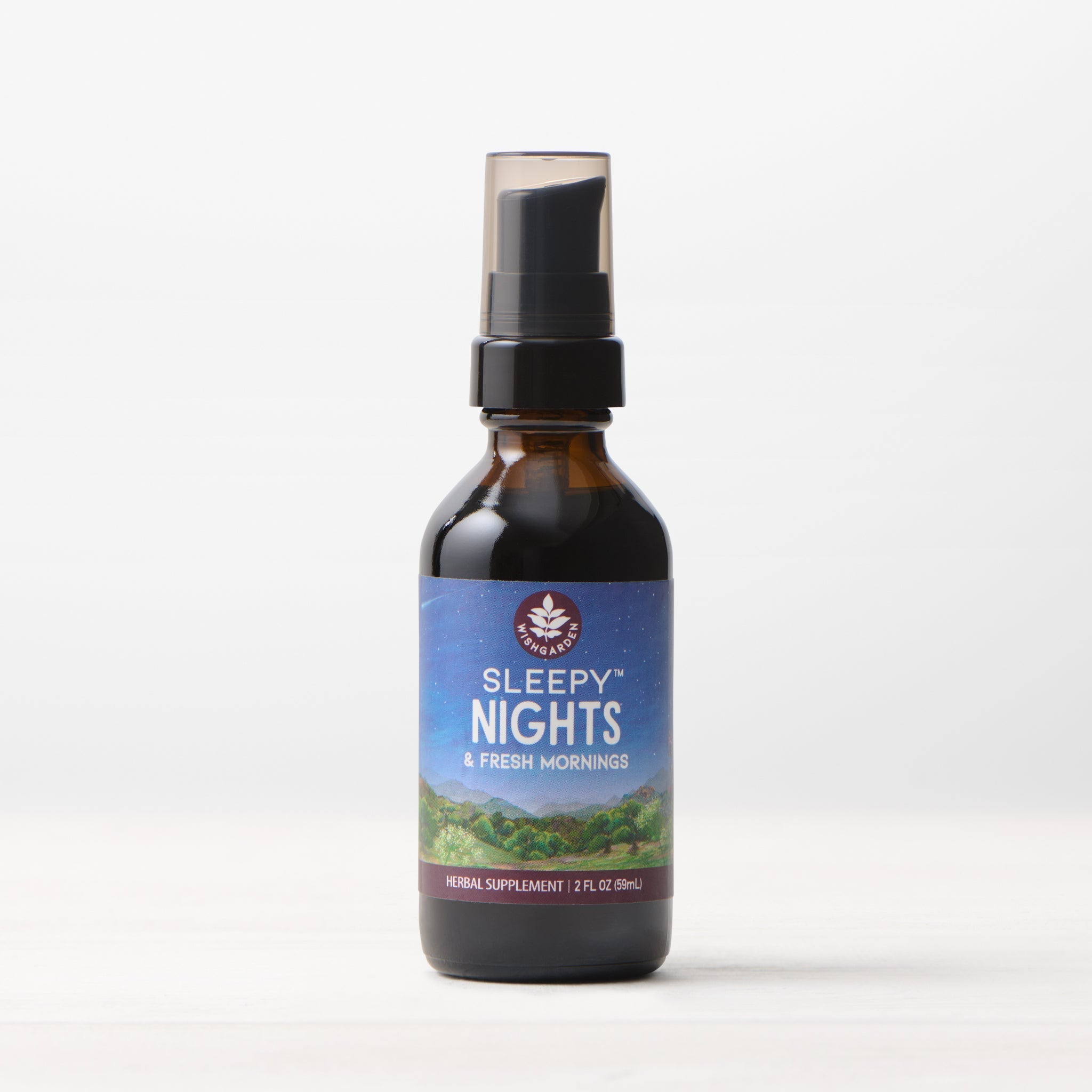 A brown glass bottle of Sleepy Nights & Fresh Mornings sleep supplement with a spray top rests on a white surface. Its label, featuring a night sky and green hills, faces forward against a light background.