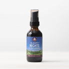 A brown glass bottle of Sleepy Nights & Fresh Mornings sleep supplement with a spray top rests on a white surface. Its label, featuring a night sky and green hills, faces forward against a light background.