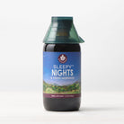 A bottle of Sleepy Nights & Fresh Mornings sleep supplement sits on a light surface, displaying a scenic label with mountains, sky, and stars, and is topped with a green, cone-shaped cap.