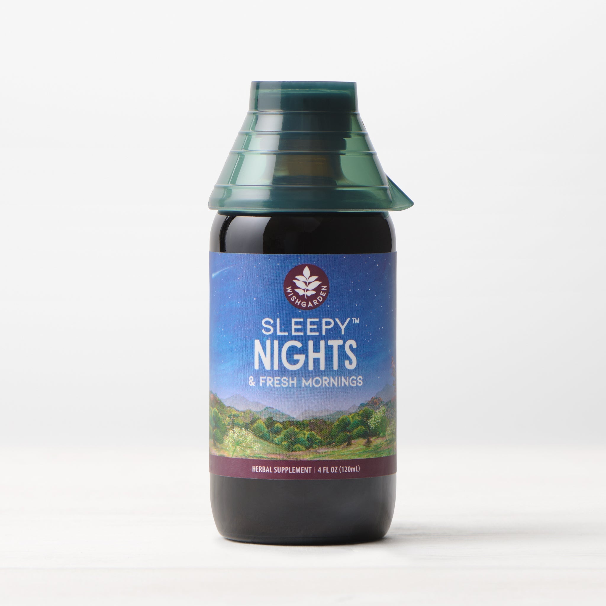 A bottle of Sleepy Nights & Fresh Mornings sleep supplement sits on a light surface, displaying a scenic label with mountains, sky, and stars, and is topped with a green, cone-shaped cap.