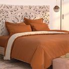 A bed features the PureCare Duvet Cover | Soft Touch Bamboo in burnt orange and cream against an ornate carved wooden headboard. A round pendant light and plush ottoman complete the softly lit, modern bedroom.