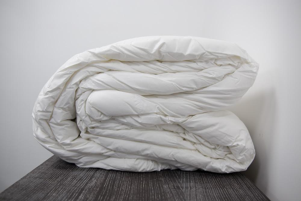 The Twovet Comforter | Couples Comforter "The Duvet for Two," an eco-friendly and hypoallergenic comforter, is neatly folded on a dark wooden surface against a plain white wall.