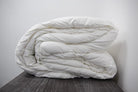 The Twovet Comforter | Couples Comforter "The Duvet for Two," an eco-friendly and hypoallergenic comforter, is neatly folded on a dark wooden surface against a plain white wall.